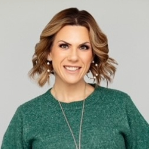 Georgina Larson Smiling person with chin length curled light brown hair wearing a green sweater and a long silver necklace